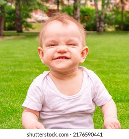 Cute laughing blonde baby girl 1 year old top having fun sitting in green grass outdoors.  Summer season. Looking at camera. Happy little child laughs nicker in meadow.