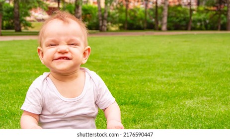 Cute laughing blonde baby girl 1 year old top having fun sitting in green grass outdoors. Childhood. Summer season. Looking at camera. Happy little child laughs nicker in meadow.