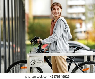 Cute Laughing Girl Parking A Bicycle On A Bike Parking Near The Market. Young Girl Smiling And Looking Into The Camera.