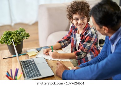 Cute Learner. Portrait Of Joyful Little Hispanic School Boy Doing Homework Together With His Father, Using Laptop While Sitting At The Desk At Home