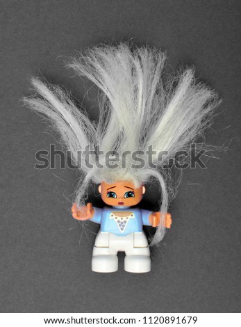 Cute Lego toy girl with a dry damaged blond hair, holding her hair and looking sad and unhappy. Concept of damaged hair, split ends, hair problems. Grey background.