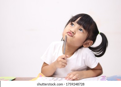 Cute Litle Asian Baby Girl Holding Pen And Book, Studying And Learning While Thinking Something Or Having Good Idea, Smiling And Looking Up, Imagination With Copy Space