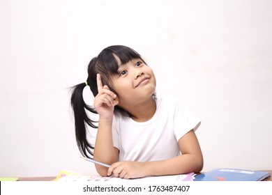 Cute Litle Asian Baby Girl Holding Pen And Book, Studying And Learning While Thinking Something Or Having Good Idea, Smiling And Looking Up, Imagination With Copy Space