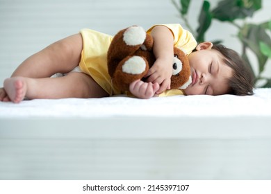 Cute little 7 months old baby girl sleeping in bed hugging a toy teddy bear in arm