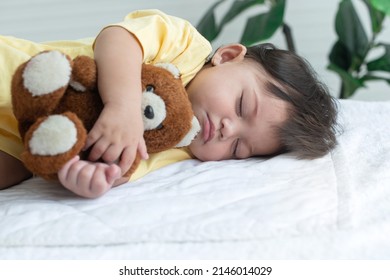 Cute little 7 months old baby girl sleeping in bed hugging a toy teddy bear in arm