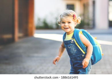 Cute little adorable toddler girl on her first day going to playschool. Healthy beautiful baby walking to nursery school and kindergarten. Happy child with backpack on the city street, outdoors.