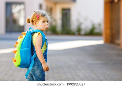 Cute little adorable toddler girl on her first day going to playschool. Healthy upset sad baby walking to nursery school. Fear of kindergarten. Unhappy child with backpack on city street, outdoors