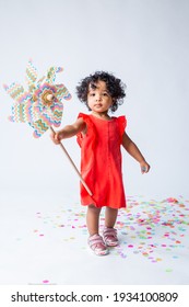 Cute Little African American Girl In Summer Clothes Holding A Baby Windmill On A White Background. The Concept Of Summer Holidays For Children