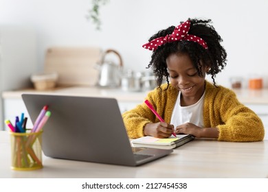 Cute Little African American Girl Study With Laptop And Writing In Notepad, Smiling Preteen Female Child Sitting At Table In Kitchen, Study Remotely With Computer At Home, Enjoying Distance Learning