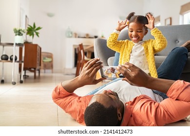 Cute little african american girl making funny face sitting on father's stomach taking photo on smartphone. Middle aged black father and daughter enjoying at home by clicking pictures in mobile phone. - Powered by Shutterstock