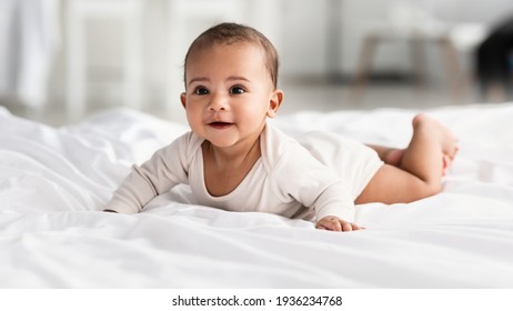 Cute little African American infant lying on white bed