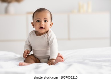 Cute little African American infant sitting on bed