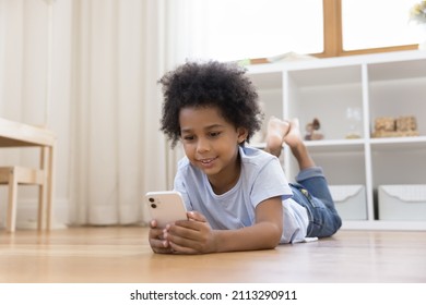 Cute Little African Boy Lying On Floor Having Fun Using Smartphone, Enjoy Amusing Cool Mobile Application, Play New Video Game, Watch Funny Online Video Vlog. Modern Tech, Gen Z Gadget Overuse Concept