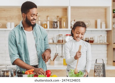 Cute little african girl helping her dad to make salad, cooking together, kitchen interior, copy space - Powered by Shutterstock