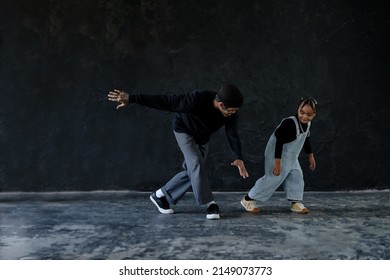 Cute little African kid boy and cool young Asian man teacher with tattoo are practice hip hop or freestyle dancing on cement floor on black background. Child education on free time
