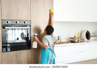 Cute little African-American boy cleaning kitchen with sponge at home - Powered by Shutterstock