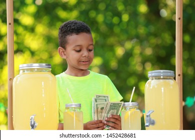 Cute Little African-American Boy With Money At Lemonade Stand In Park. Summer Refreshing Natural Drink