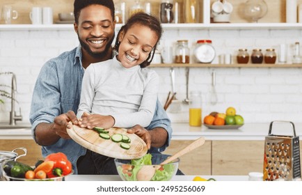 Cute little afro girl and his father making salad together. Happy childhood concept, copy space - Powered by Shutterstock