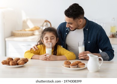 Cute Little Arab Girl Enjoying Drinking Milk While Having Snacks With Daddy In Kitchen, Happy Young Middle Eastern Dad Father And Daughter Sitting At Table, Having A Bite Together, Free Space - Powered by Shutterstock