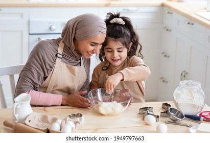 Cute Little Arab Girl Helping Her Muslim Mom In Kitchen, Baking Homemade Cookies Together, Female Child Adding Ingredients To Bowl With Dough, Enjoying Cooking With Mother, Closeup Shot