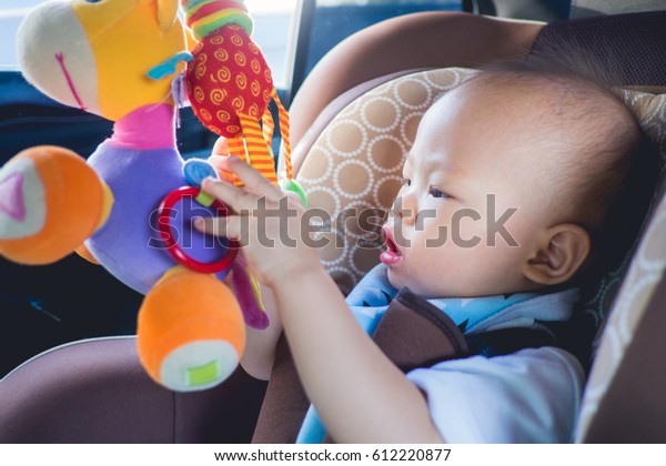 Cute little Asian 1 year old toddler baby boy\
child trying to reach colorful toy, Kid sitting & playing toy\
in car seat, toddler is having fun, Happy little traveler safety,\
road trip concept