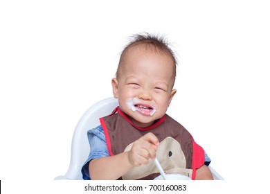 Cute Little Asian 18 Months / 1 Year Old Toddler Baby Boy Child Eating Yogurt. Dirty Face Of Funny Kid. Smiling Toddler Eating With A Stained Face, Self Feeding Concept - Isolated On White