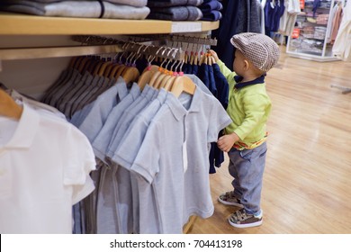 Cute Little Asian 18 Months / 1 Year Old Toddler Baby Boy Child Choosing Kids Clothes In Garments Shop,  Shopping. Kid's Fashion. Modern Children Concept