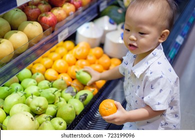 Cute Little Asian 18 Months / 1 Year Old Toddler Baby Boy Child Shopping In A Supermarket. Kid Standing Choosing And Holding Fruit In Grocery Store, Kid First Experience Concept - Selective Focus