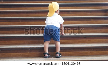 Cute little Asian 18 months / 1.7 year old toddler baby boy child climbs up the wooden stairs with the Mind your step sticker sign. Kid trying to walk up staircase concept.