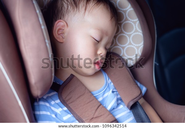 Cute little Asian 18 months / 1 year toddler baby\
boy child sleeping in modern car seat. Child traveling safety on\
the road. Safe way to travel fastened seat belts in vehicle with\
young kid concept