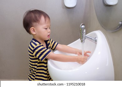 Cute Little Asian 2 Years Old Toddler Baby Boy Child Washing Hands By Himself On White Sink And Water Drop From Faucet In Public Toilet / Bathroom For Kids, Sanitation / Hygiene Concept