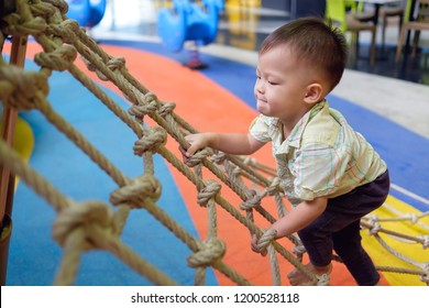 Cute little Asian 2 years old toddler baby boy child having fun trying to climb on jungle gym at indoor playground, Physical, Hand and Eye Coordination, Sensory, Motor Skills development concept