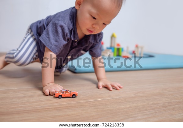 Cute little Asian 20 months / 1 year old toddler baby\
boy child playing with toy car in living room at home, selective\
focus at orange small toy car, Kid under 3 years old play with\
small parts toy