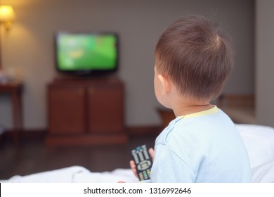 Cute Little Asian 2-3 Years Old Toddler Baby Boy Child Sitting In Bed Holding The Tv Remote Control And Watching Television In Bedroom At Home, Toddlers Screen Time & Early Brain Development Concept