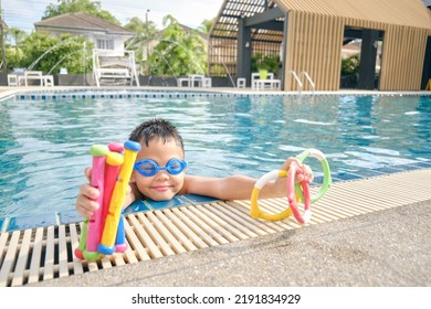 Cute Little Asian 6 Years Old School Boy Child Wear Swimming Goggles Learning To Swim With Diving Pool Underwater Swimming Toys, Diving Sticks, Diving Rings Toy For Kids At Outdoor Pool In Summer Day