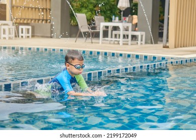 Cute Little Asian 6 Years Old School Boy Child In Swimming Goggles And Swimming Suit Learning To Swim At Outdoor Pool In Summer Day, Happy Kid Having Fun On Summer Vacation