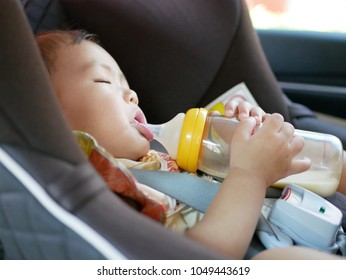 Cute Little Asian Baby Girl, 11 Months Old, Falling Asleep With Her Hands Holding A Milk Bottle On A Car Seat While Traveling With Her Parents By Car