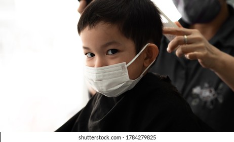 Cute Little Asian Boy  With Protective Mask And Barber Man Or Parent With Protective Mask Doing A Hair Cut In The Quarantine At Home Covid-19