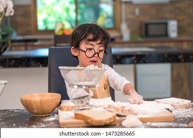 Cute Little Asian Boy Sifting Dough Flour With Sifter Sieve Colander In Home Kitchen For Prepare To Baking Bakery And Cake. Thai Kids Playing With Flour As Chef Funny. People Child Playing