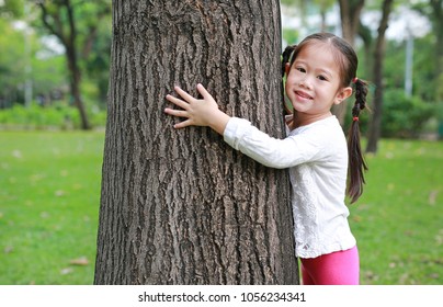 Cute Little Asian Child Girl Hugging A Big Tree In The Garden.