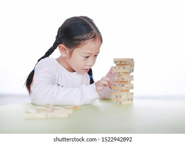 Cute Little Asian Child Girl Playing Wood Blocks Tower Game For Brain And Physical Development Skill In A Classroom. Focus At Children Face. Kid Imagination And Learning Concept.