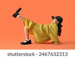 Cute little Asian girl in adult clothes on orange background