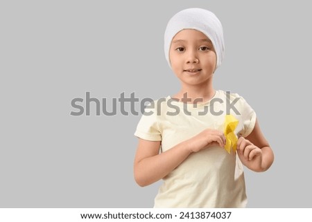 Cute little Asian girl after chemotherapy with yellow ribbon on grey background. Childhood cancer awareness concept