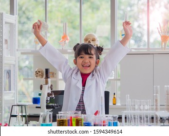 Cute Little Asian Girl Cheerfully Raise Up Both Hands With Big Smile. Kid Playing Scientist Or Doctor Roll In The Laboratory. Science Class And Children Day Concept.