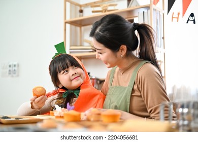 Cute Little Asian Girl In Halloween Costume Happy To Make A Halloween Cupcakes With Her Mom At Home. Happy Family In Halloween Seasons.