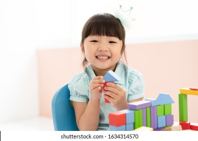 Cute Little Asian Girl Playing With Colorful Toy Blocks While Sitting At Table And Smiling At The Camera. Educational And Creative Toys And Games For Young Children. Child At Home.