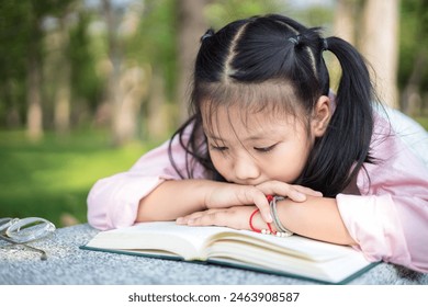 Cute little asian girl reading a book while lying at garden - Powered by Shutterstock