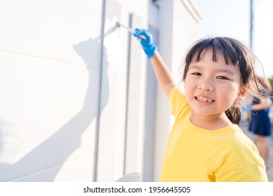 Cute Little Asian Kid Girl Painting On Wall Cement Fence Outdoor.Volunteer Kid Project Painting Wall In Local School.renovate.kid Holding Brush.renew House.Paint Color.Home, Community Service.charity.