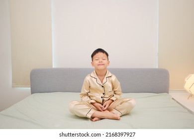 Cute Little Asian Kindergarten Boy Child With Closed Eyes Sitting On Bed And Practicing Meditation In The Morning After Waking Up In Bedroom At Home,  Beginner Meditation, Breathing Exercise For Kids