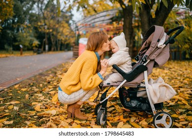 Cute little baby with big blue eyes, short red hair, pump lips in a stroller outside in the fall with nice happy mum sits near it